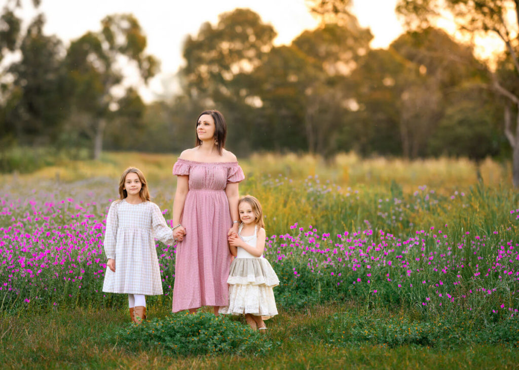 mum holding her 2 daughters during outdoor family session at a location in Melbourne with pink flowers.