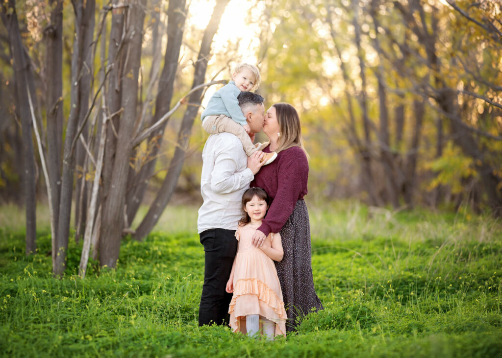 Melbourne parents kissing while holding kids during outdoor family photoshoot